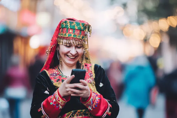 A cheerful woman in traditional clothing using her smartphone during a festive moment, showing how easily the 10WIN app fits into everyday life.